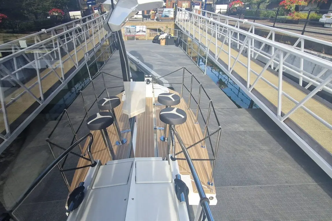 View from above of a boat dock showing a wooden deck, black stools, and a modern walkway leading to a nearby dock.